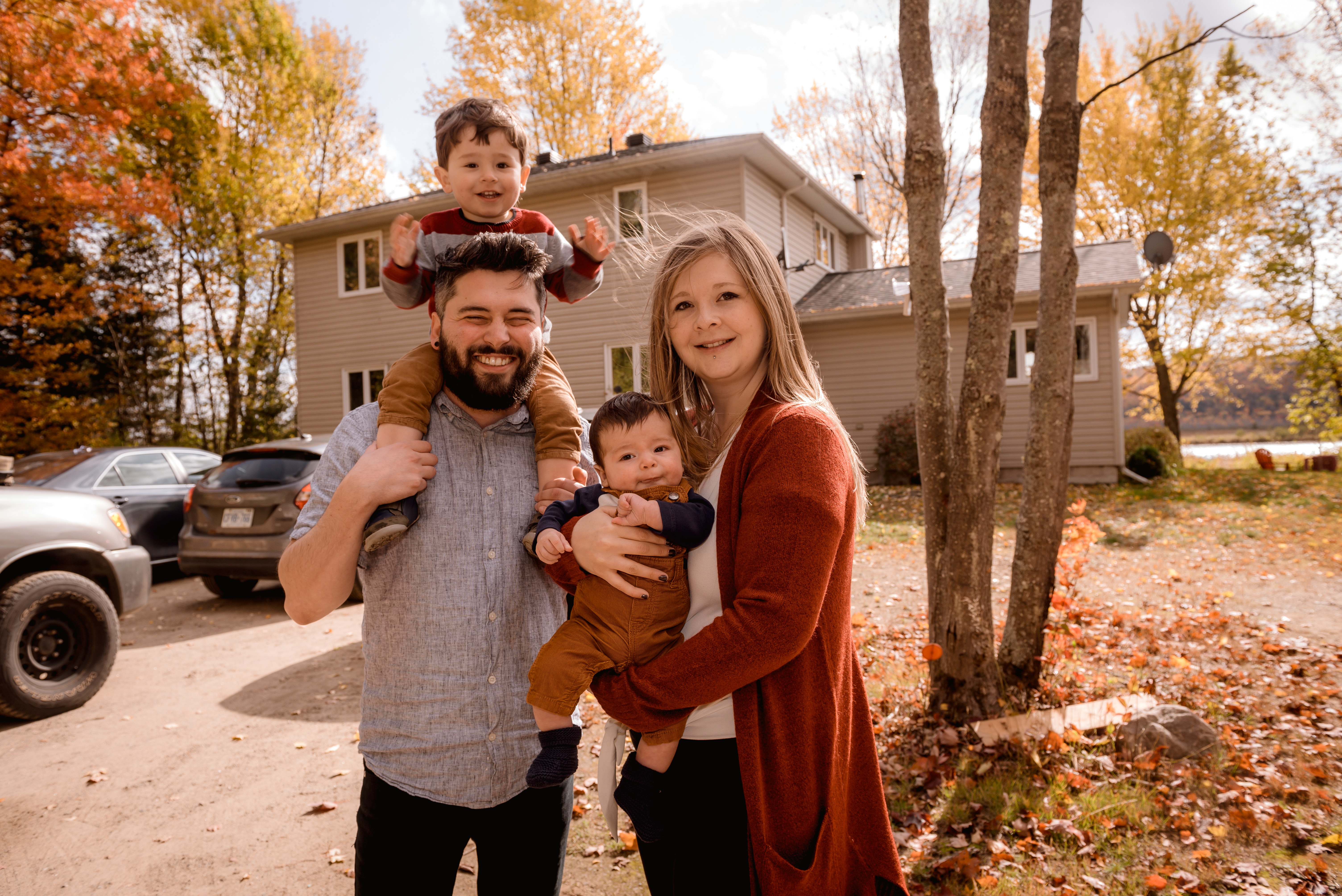 family of 4 standing outside of home with multiple of parked cars
