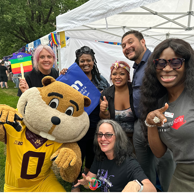 Staff and mascot smiling and pointing at camera